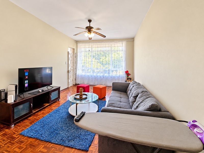 A comfortable living room featuring classic parquet flooring, a ceiling fan, and a large window that allows for natural light.