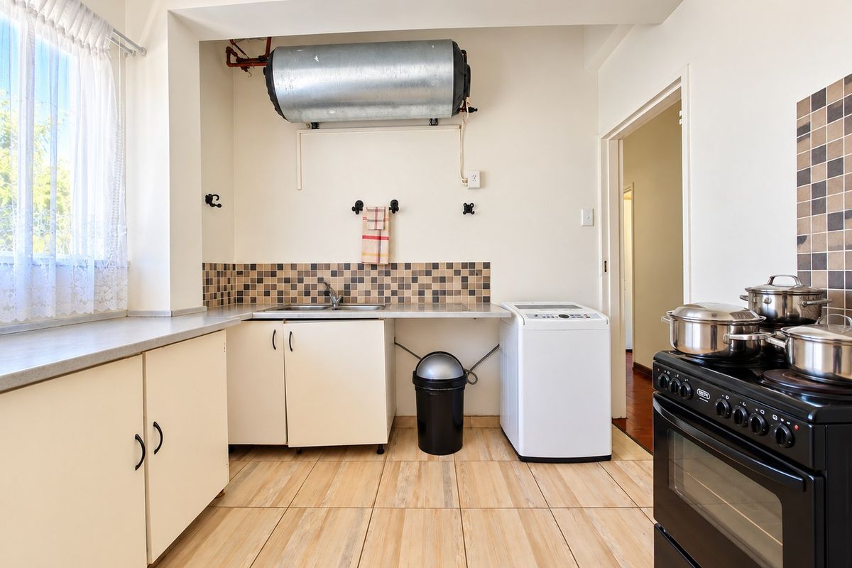 A functional kitchen featuring tiled flooring, built-in cabinetry, a stainless steel sink, and an electric stove with a wall-mounted geyser.