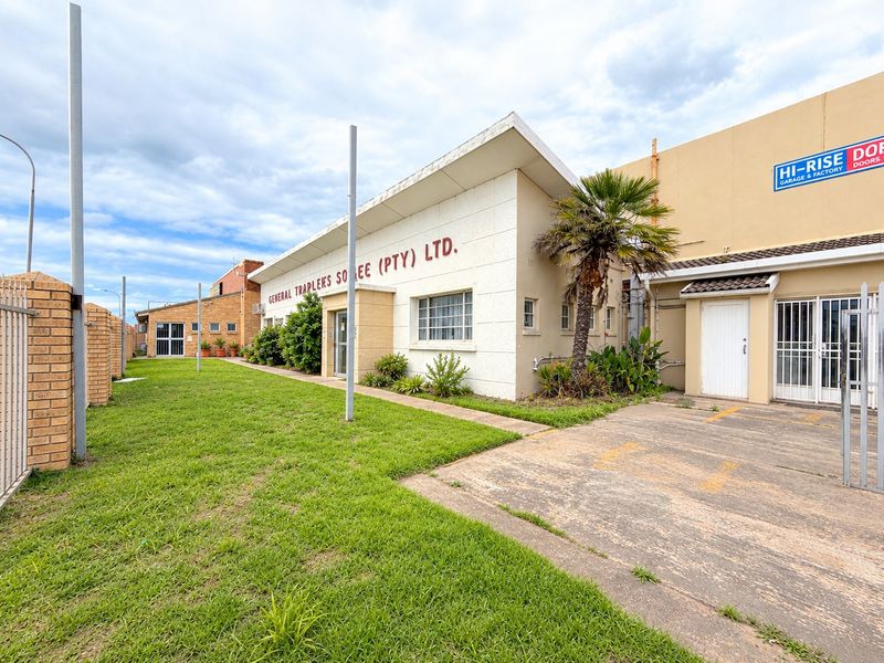 Front exterior view of an industrial property featuring a concrete driveway, security fencing, and a prominent building facade with signage.