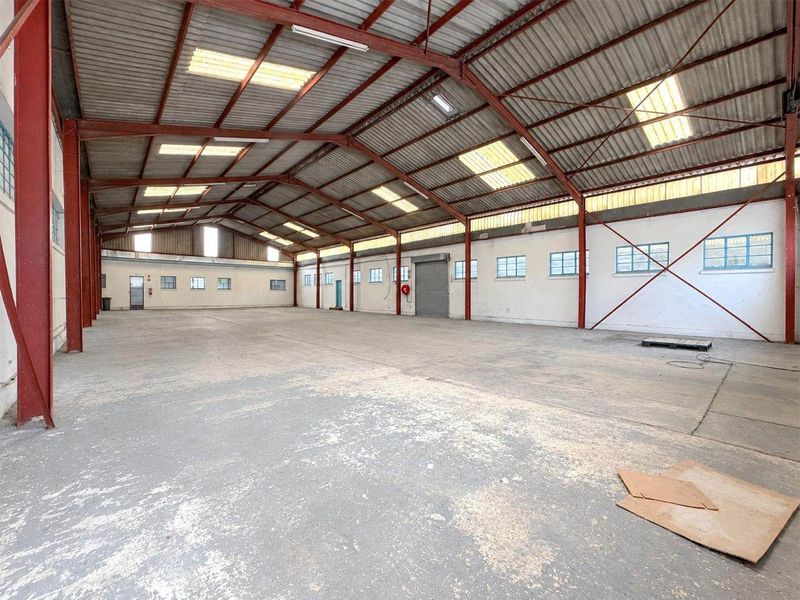 Spacious industrial warehouse featuring a high-clearance steel portal frame, concrete flooring, natural light via skylights, and a large roller shutter door for easy access.
