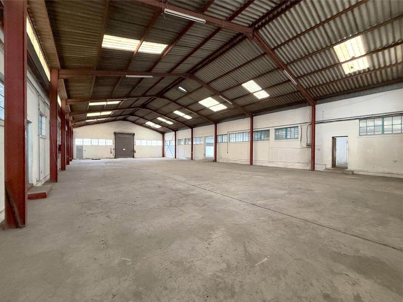 Spacious industrial warehouse featuring a high-clearance steel portal frame, concrete flooring, natural light via skylights, and a large roller shutter door for easy access.