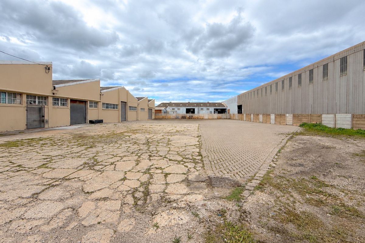 Spacious industrial yard area featuring a mix of concrete and paved surfaces, flanked by multiple warehouse structures with roller shutter access.