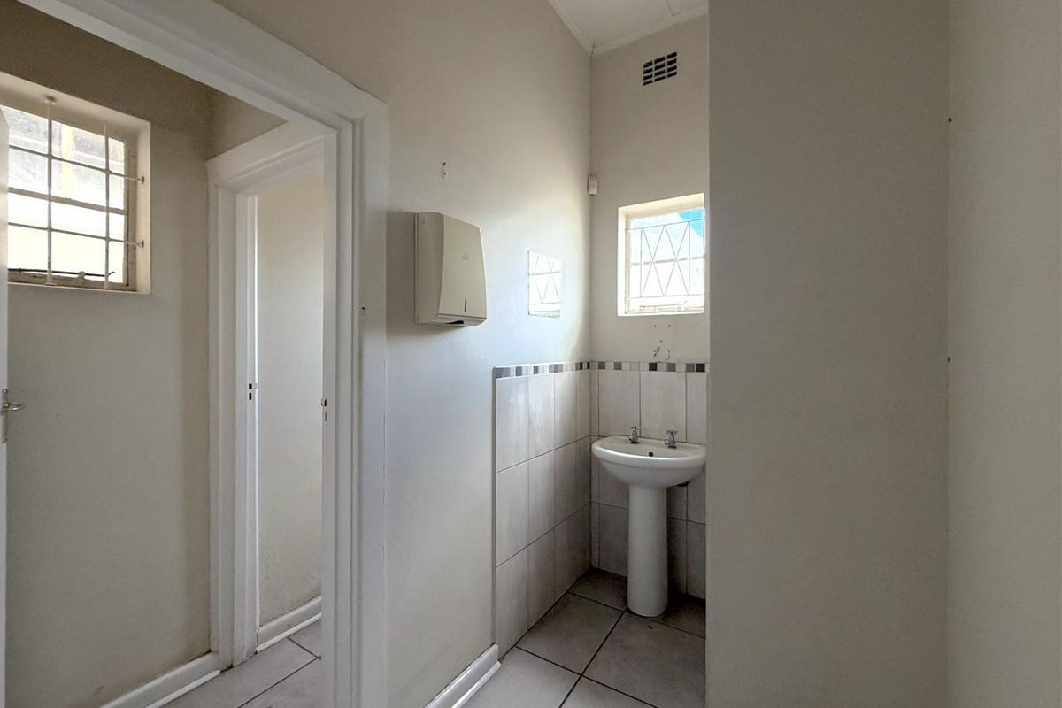 A functional bathroom space featuring a pedestal basin, tiled flooring, and partial wall tiling, with security bars on the windows.