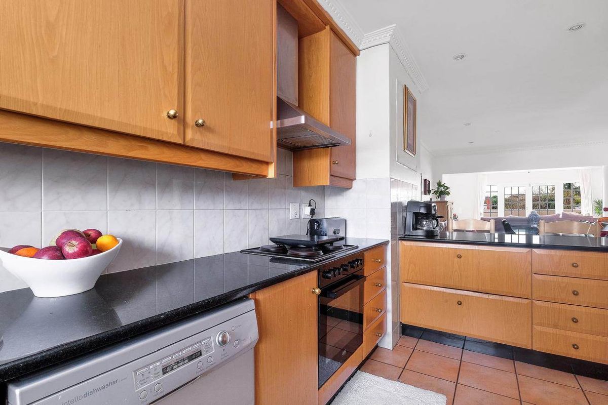 A functional kitchen featuring wooden cabinetry, granite countertops, built-in oven, hob, and extractor fan, with a tiled backsplash and flooring.