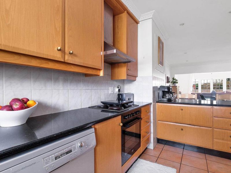 A functional kitchen featuring wooden cabinetry, granite countertops, built-in oven, hob, and extractor fan, with a tiled backsplash and flooring.