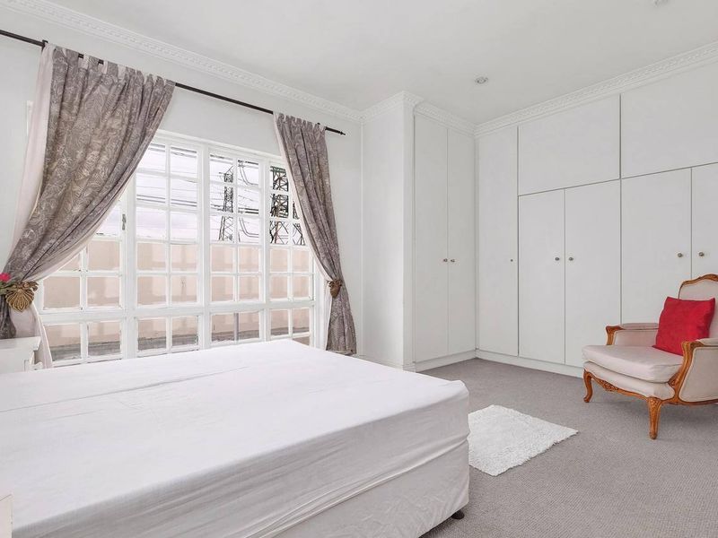 A bright bedroom featuring extensive built-in floor-to-ceiling cupboards, classic crown molding, and a large grid-pattern window allowing for natural light.