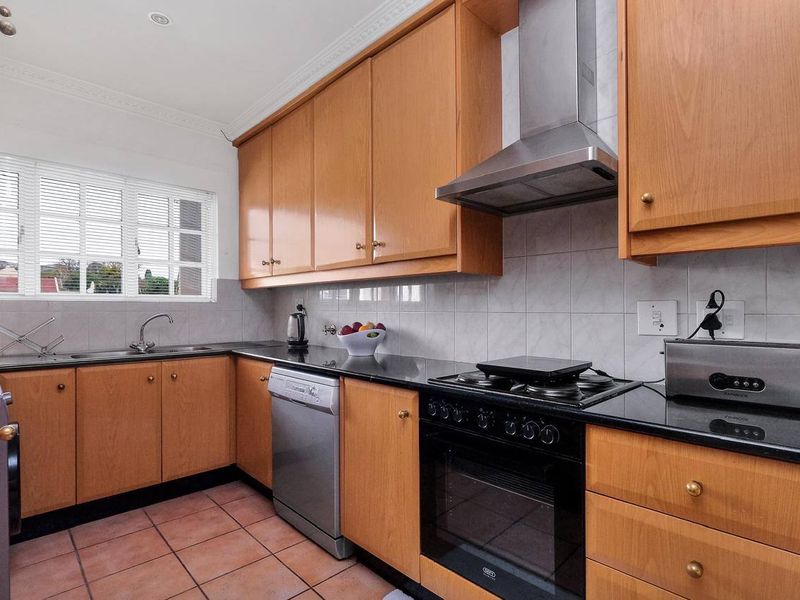 A functional kitchen featuring wooden cabinetry, granite countertops, a gas hob, built-in oven, stainless steel extractor fan, and terracotta floor tiles.