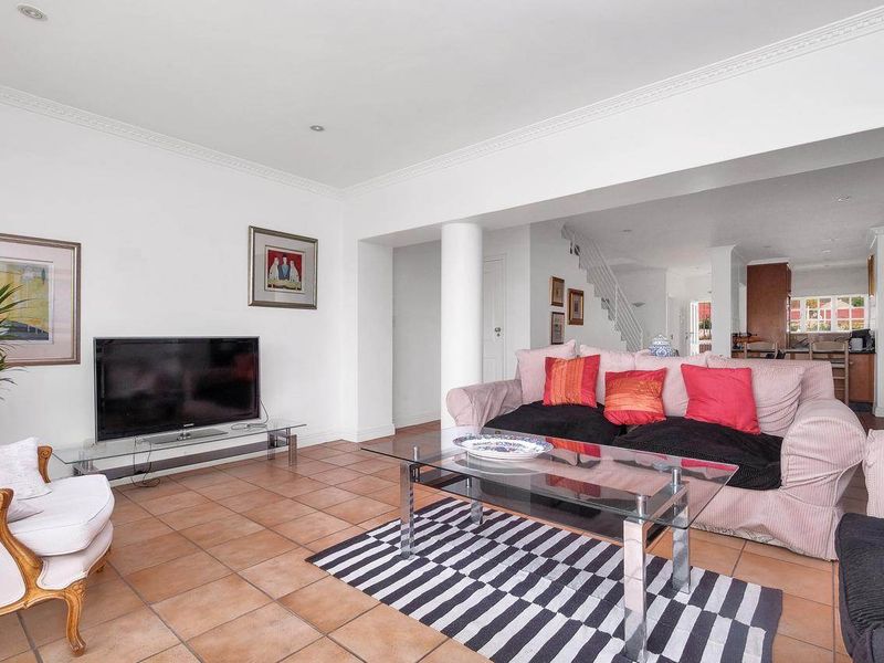 Spacious open-plan living area featuring terracotta floor tiles, crown molding, and a central structural column, with a view toward the kitchen and staircase.