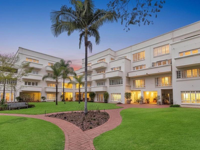 A well-maintained apartment complex featuring a central landscaped garden, paved pathways, and multiple levels of private balconies.