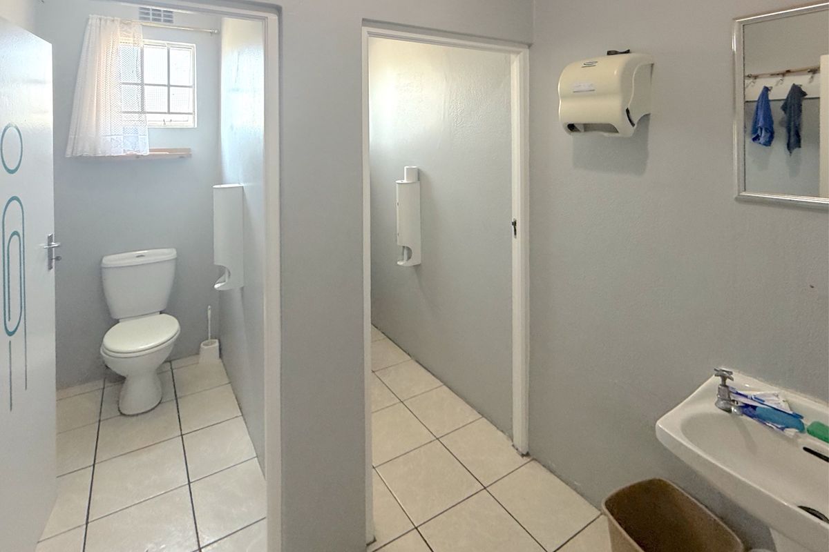 Commercial bathroom facility featuring tiled flooring, a wall-mounted basin, and separate toilet cubicles with functional fixtures.
