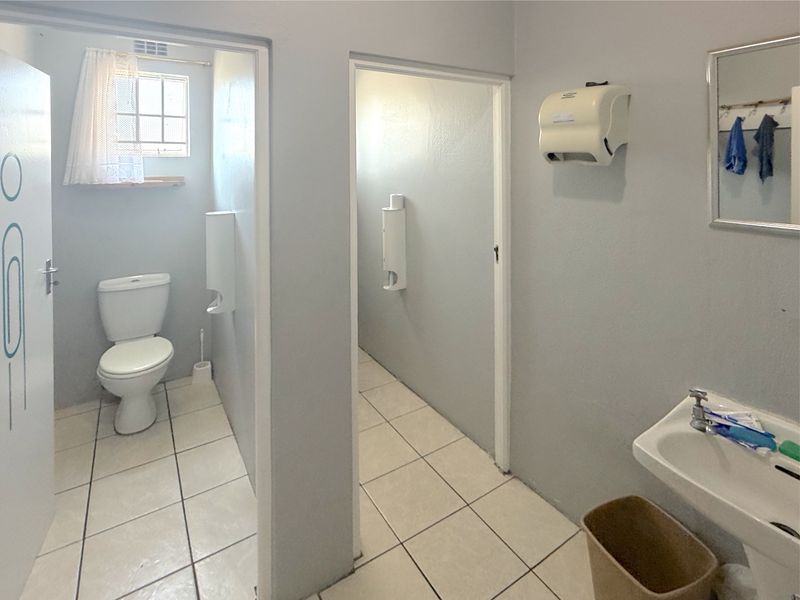 Commercial bathroom facility featuring tiled flooring, a wall-mounted basin, and separate toilet cubicles with functional fixtures.
