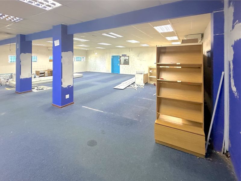 Spacious open-plan commercial office area featuring a suspended ceiling, recessed lighting, and carpeted flooring, currently in need of cosmetic refurbishment and wall repairs.