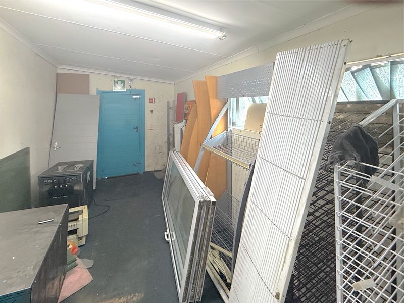 A utility or storage space featuring fluorescent lighting and an emergency exit door, currently used for storing various fixtures and materials.