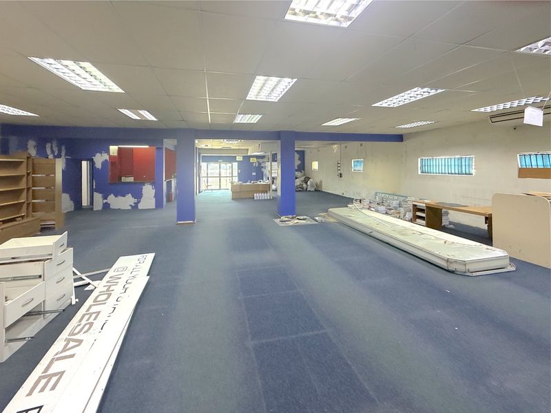 Spacious open-plan commercial interior featuring a suspended ceiling, recessed lighting, and carpeted flooring, currently vacant and requiring cosmetic refurbishment.