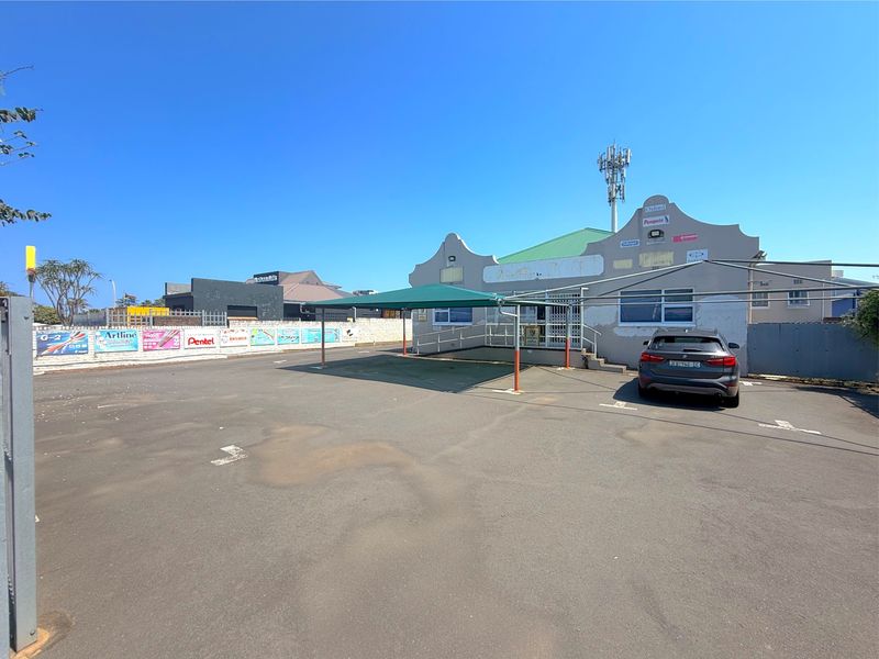 Commercial property exterior featuring an asphalt parking area, a covered carport, ramp access, and a telecommunications mast mounted on the roof.