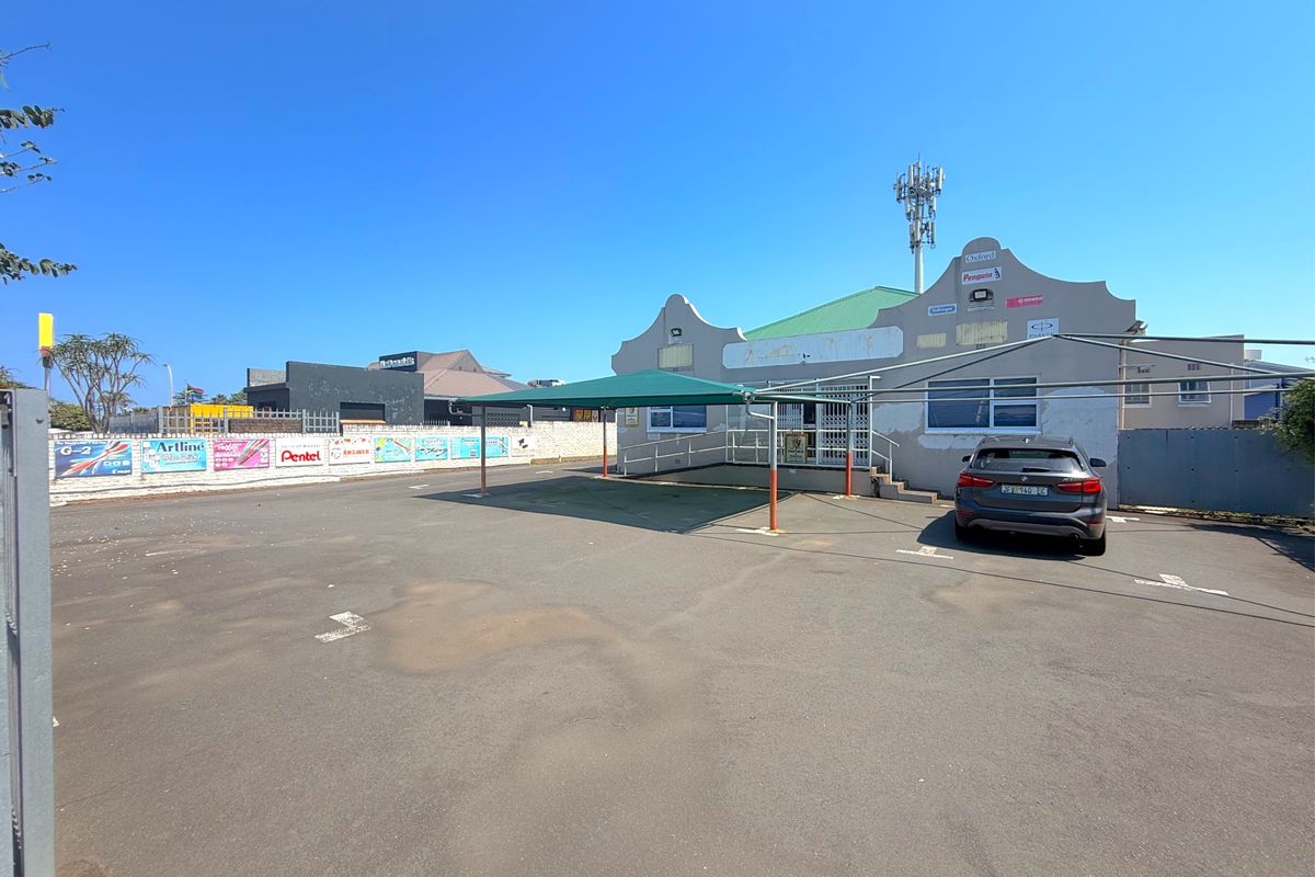 Commercial property exterior featuring an asphalt parking area, a covered carport, ramp access, and a telecommunications mast mounted on the roof.