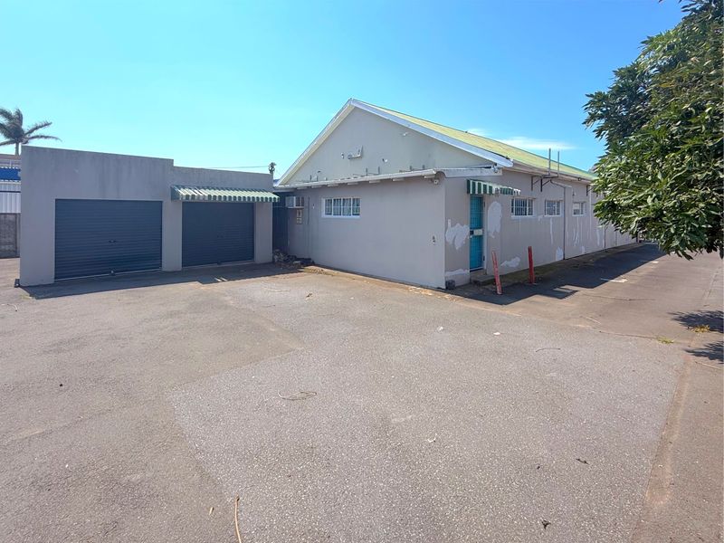 Rear exterior view of the commercial property featuring a double garage, asphalt parking area, and building facade with visible paint wear.