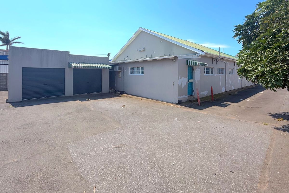 Rear exterior view of the commercial property featuring a double garage, asphalt parking area, and building facade with visible paint wear.