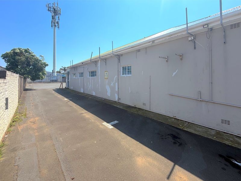 Rear exterior view of the commercial property featuring an asphalt driveway and a building facade with visible paint deterioration.