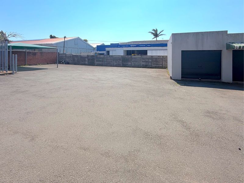 A paved commercial yard area featuring a boundary wall, a roller shutter door access point, and a shade cloth carport structure.