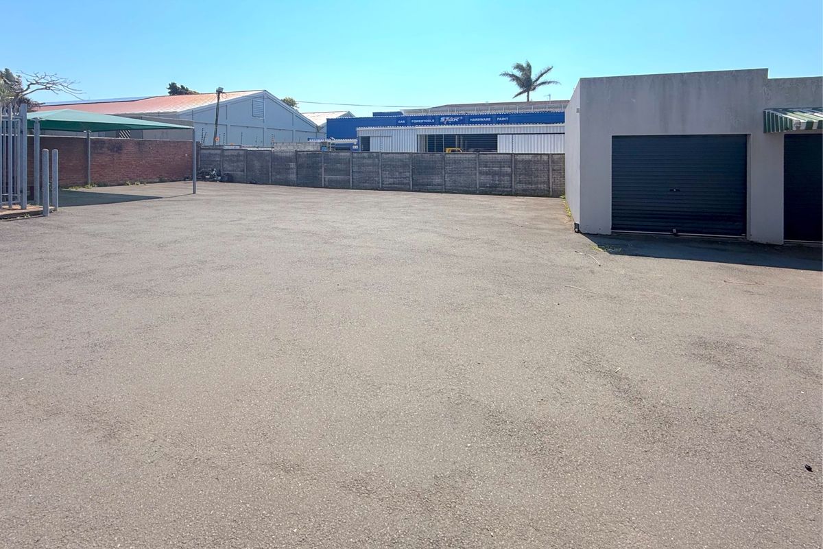 A paved commercial yard area featuring a boundary wall, a roller shutter door access point, and a shade cloth carport structure.