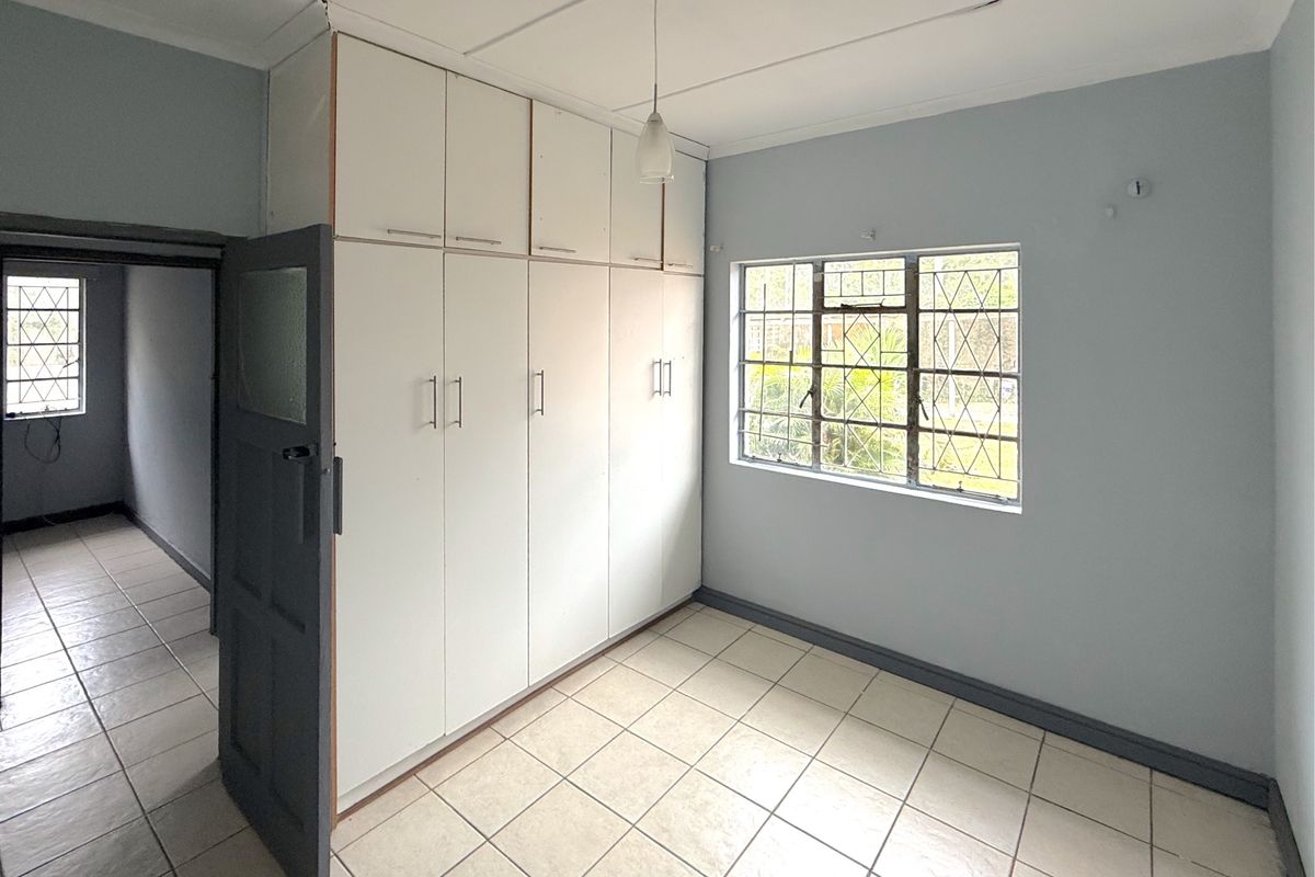 A bright, empty bedroom featuring built-in cupboards, tiled flooring, and security bars on the windows, offering a clean canvas for personalization.