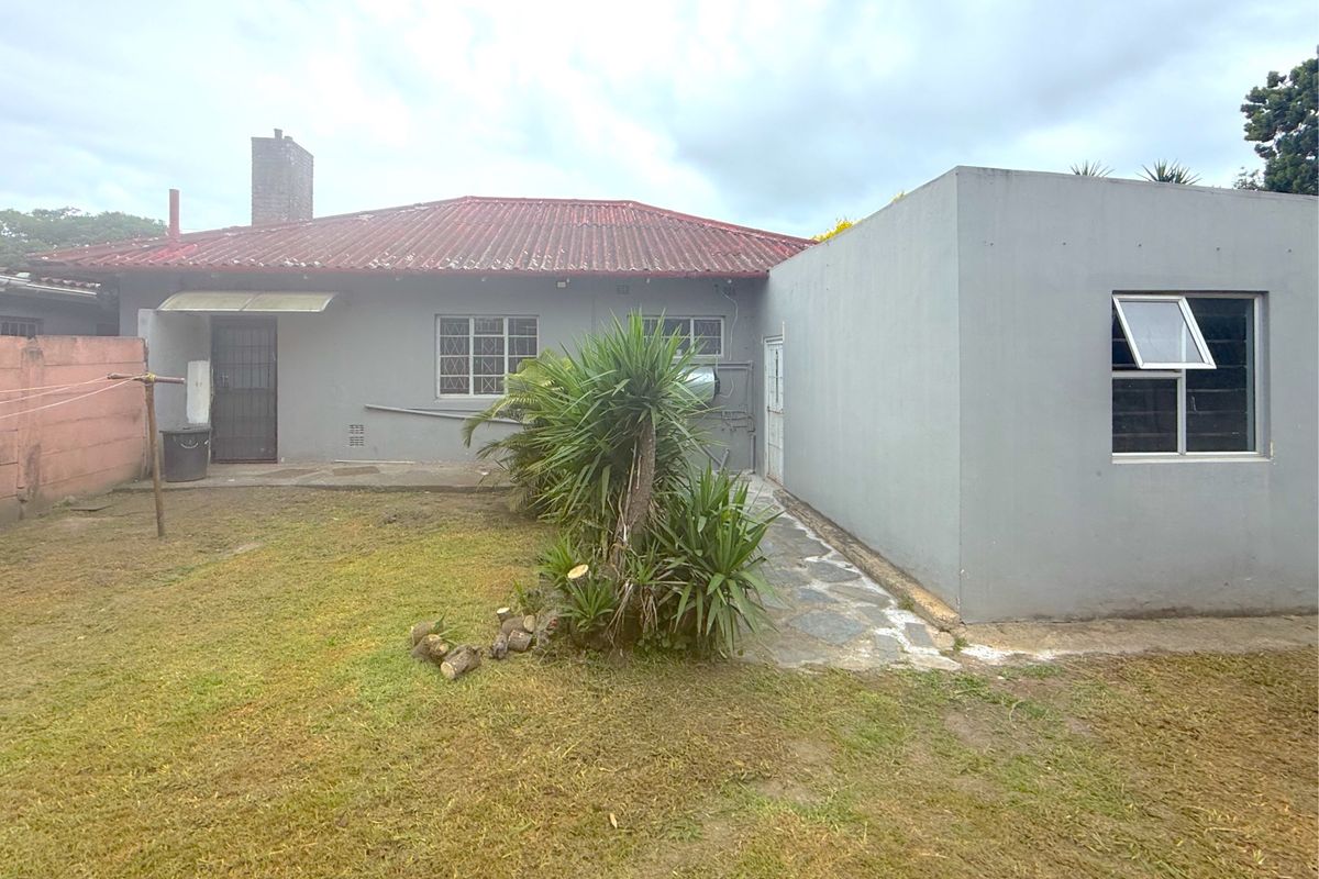 Rear view of the property featuring a tiled roof, chimney, and a small garden area with a concrete pathway.