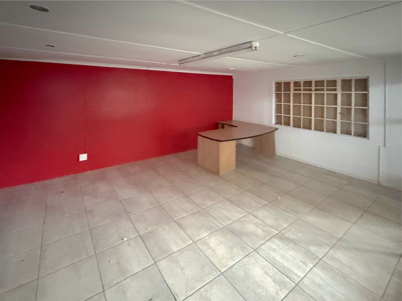 A vacant commercial office space featuring tiled flooring, a red accent wall, and a grid-style window, suitable for various business configurations.