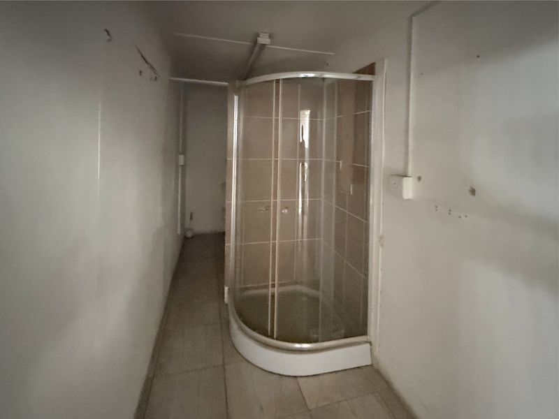 A compact bathroom featuring a curved glass shower enclosure with tiled surround and tiled flooring, requiring cosmetic updates to the walls and electrical fixtures.