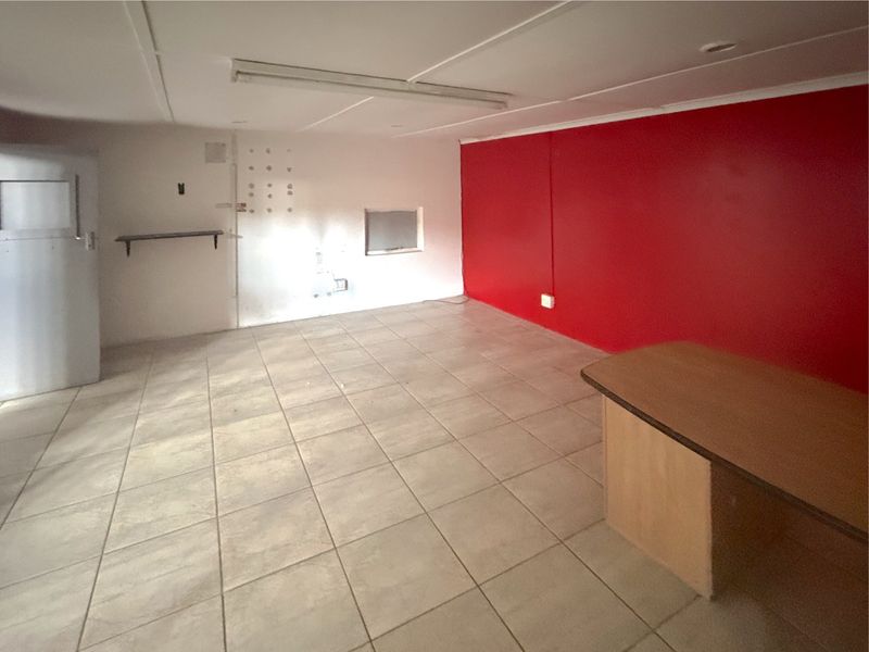 An empty commercial office space featuring tiled flooring, a bold red accent wall, and a built-in service counter.