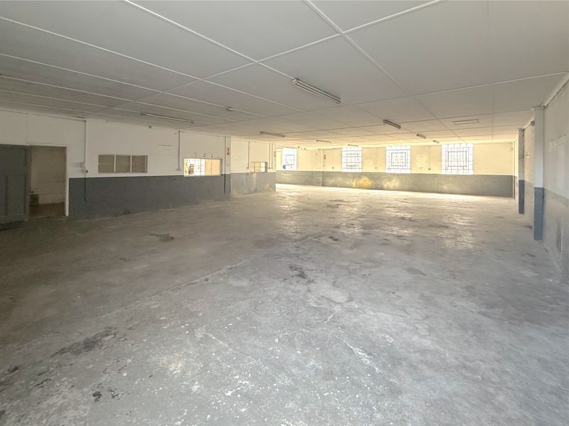 A large, open-plan commercial utility space featuring concrete flooring, suspended ceilings, and security-barred windows, suitable for warehouse or workshop use.