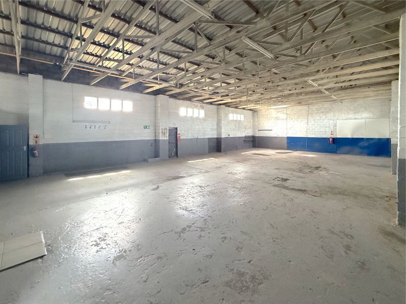 Spacious industrial utility area featuring exposed steel roof trusses, concrete flooring, and painted block walls, suitable for storage or workshop use.