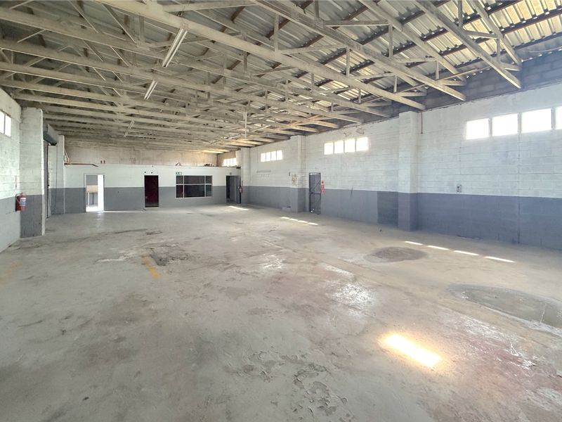 Spacious industrial utility area featuring exposed steel roof trusses, concrete flooring, and cinder block walls, suitable for warehouse or workshop use.