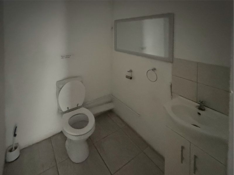 A functional commercial bathroom featuring a standard toilet, vanity basin with storage, and tiled flooring, requiring cosmetic updates to improve its overall presentation.