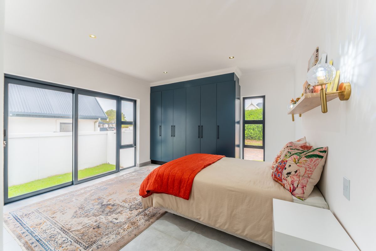 Modern bedroom featuring large sliding glass doors, built-in dark blue cabinetry, recessed ceiling lighting, and tiled flooring with direct access to the garden.
