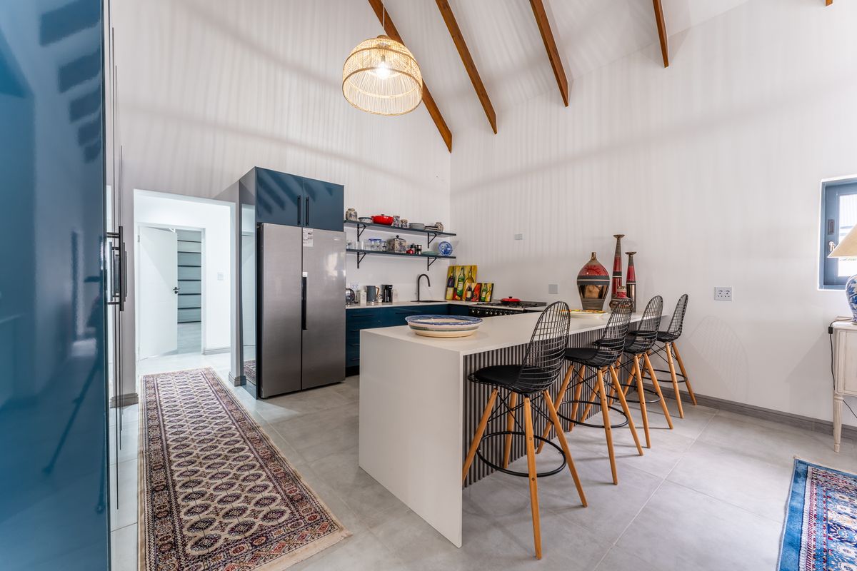 Modern kitchen featuring a central island with breakfast bar seating, exposed timber ceiling beams, and sleek blue cabinetry.