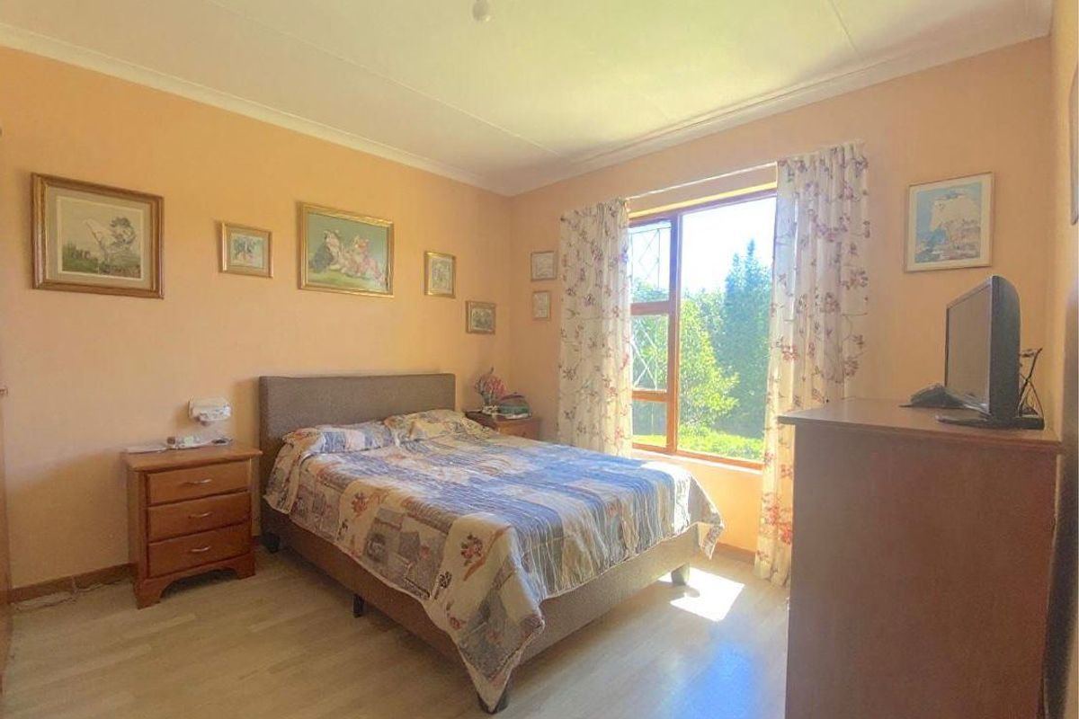 A bedroom featuring light-toned laminate flooring, peach-colored walls, and a large window providing natural light and garden views.