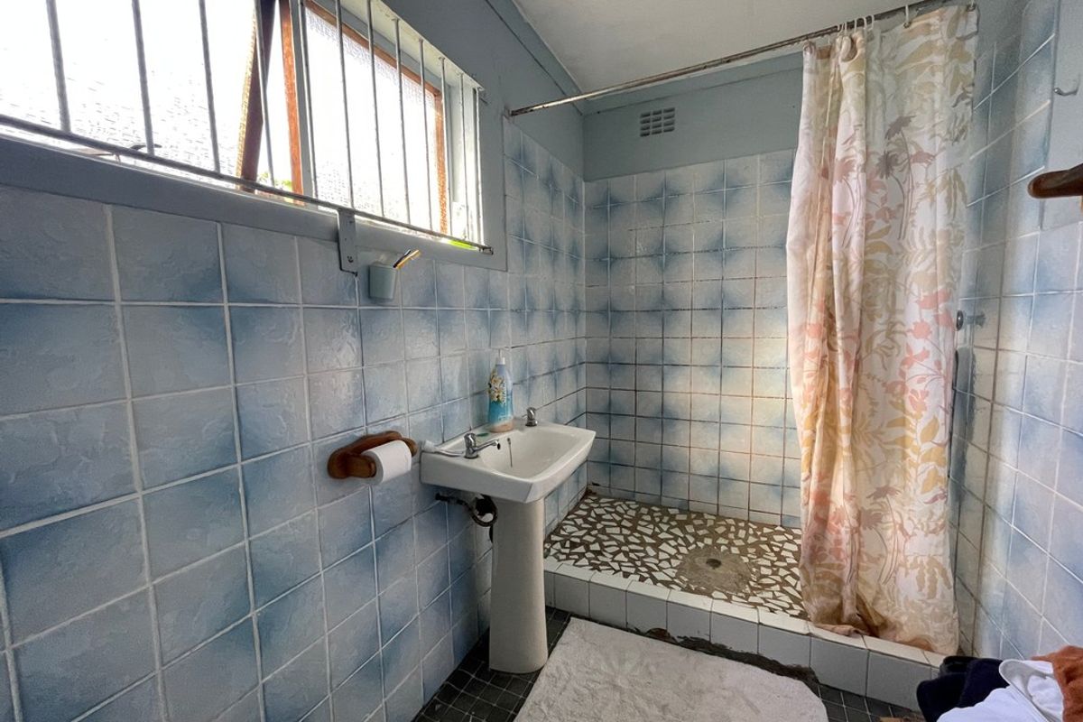A dated bathroom featuring a pedestal basin, walk-in shower area with tiled base, and security bars on the window.