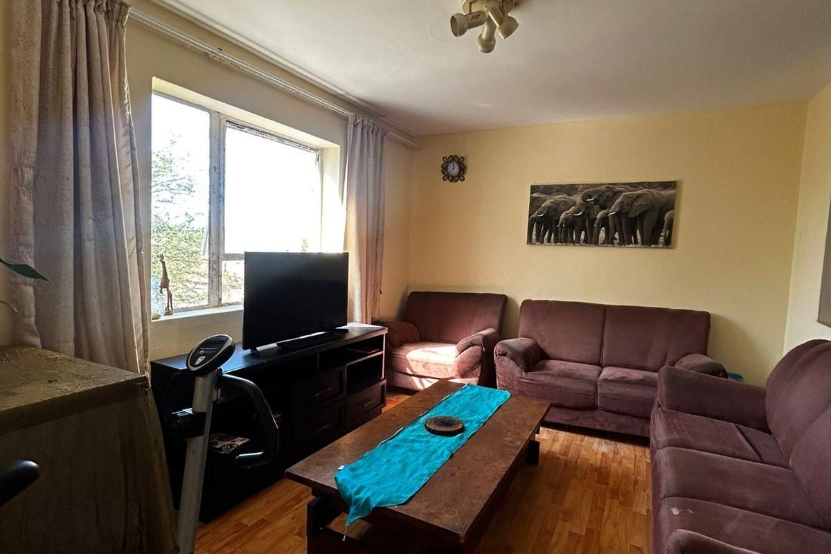A living room featuring wood-look laminate flooring, large window with natural light, and standard ceiling lighting.