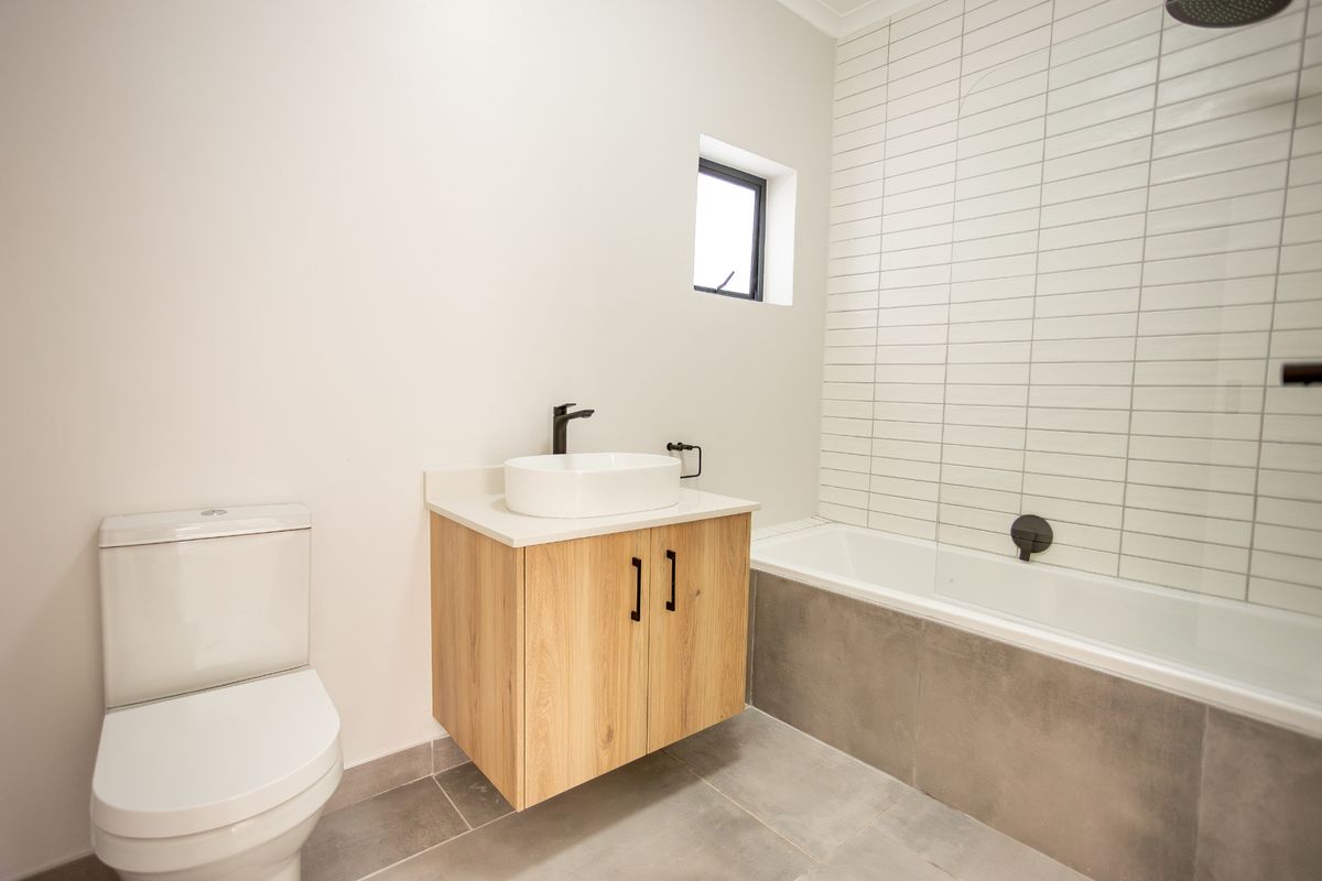 Modern bathroom featuring a floating wood-finish vanity, white vessel sink, bathtub with tiled surround, and contemporary matte black fixtures.