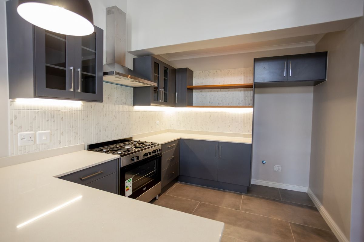Modern kitchen featuring dark grey cabinetry, stone countertops, tiled backsplash, integrated lighting, and a stainless steel gas stove with extractor fan.