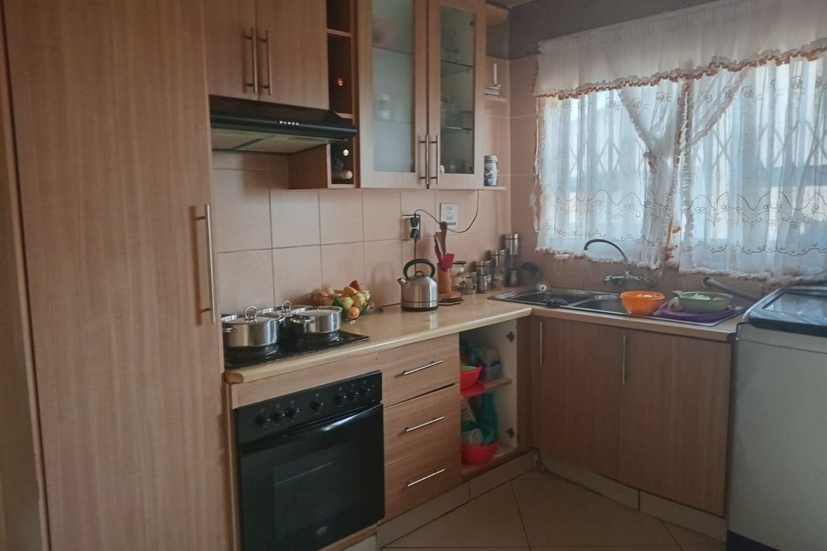 A functional kitchen featuring light wood-finish cabinetry, a built-in oven with hob, extractor fan, and a double-basin sink with tiled splashbacks.