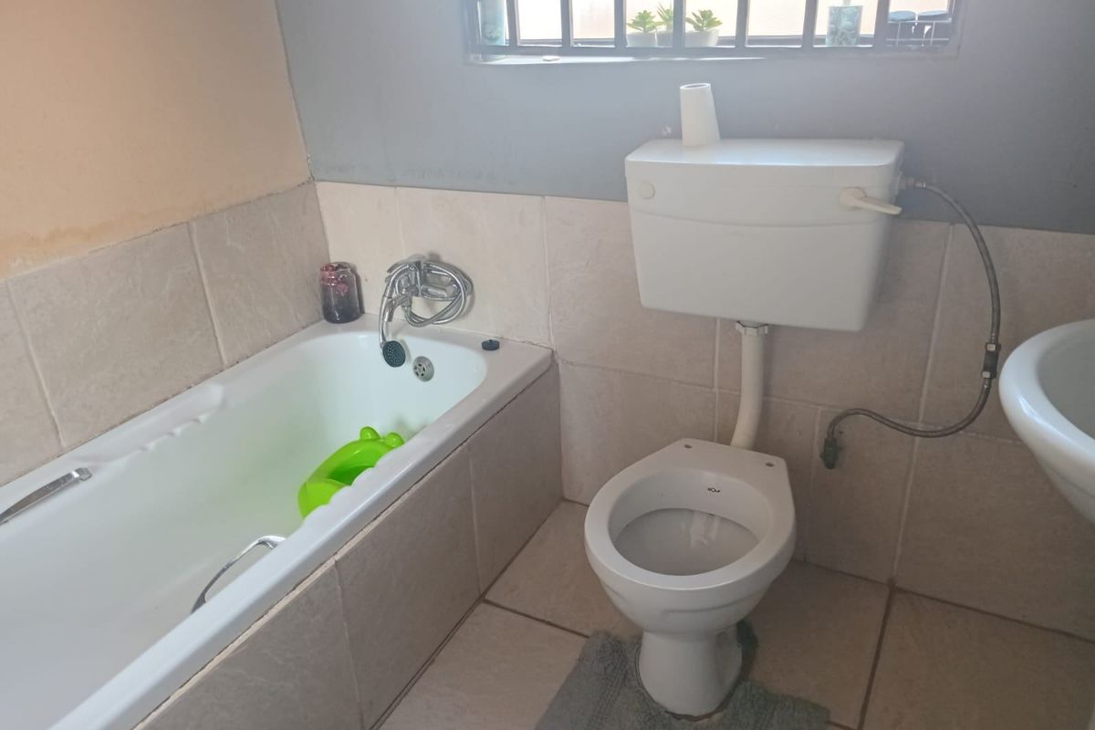 A functional bathroom featuring a built-in bathtub, standard toilet, and basin with tiled walls and flooring, requiring some cosmetic updates.