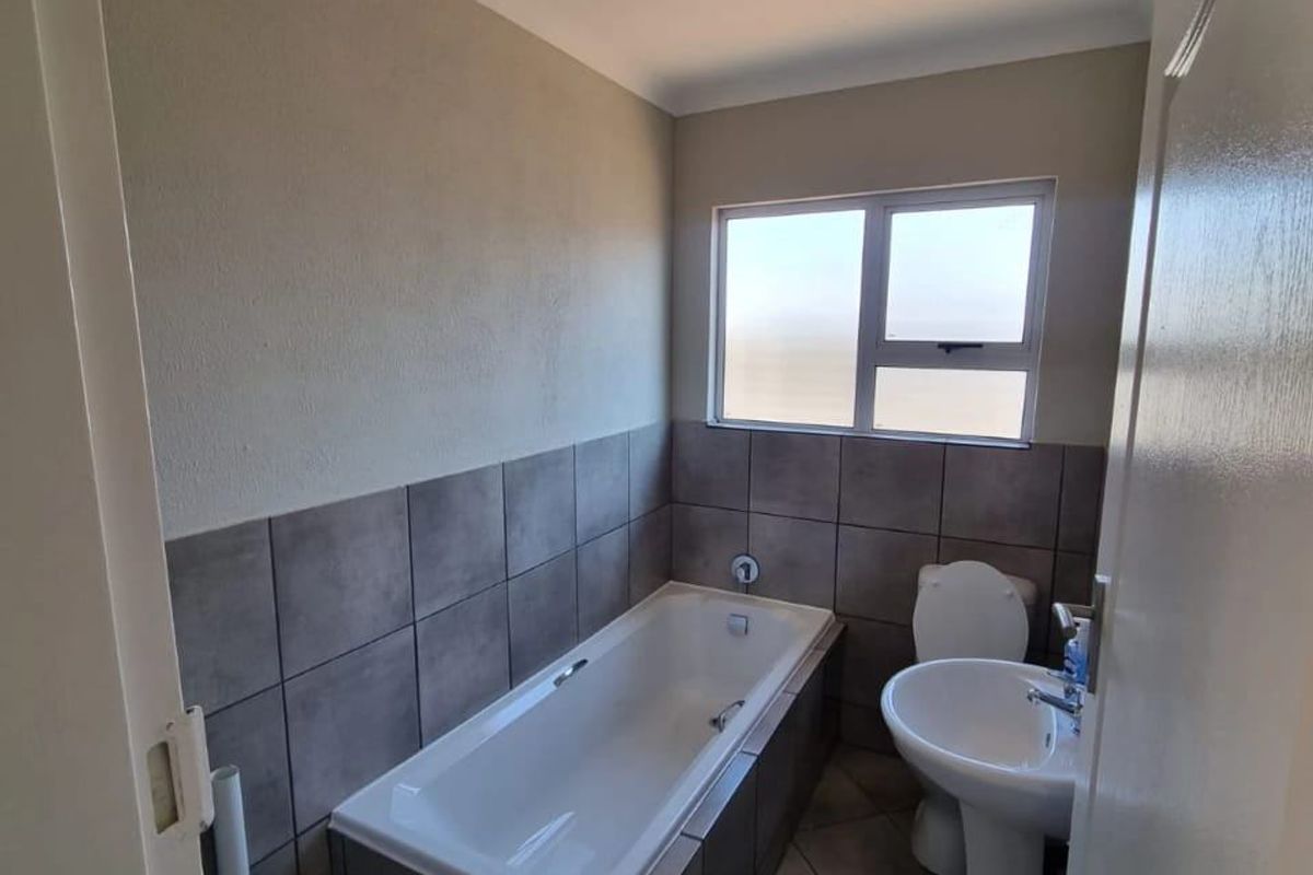 A functional bathroom featuring a built-in bathtub with tiled surround, a pedestal basin, and a toilet, finished with neutral wall and floor tiles.