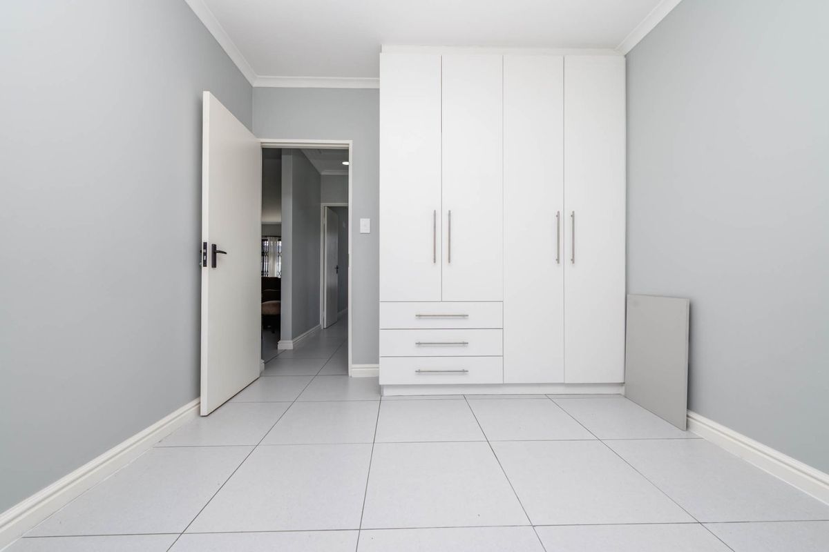 A clean, neutral bedroom featuring built-in white cabinetry with integrated drawers and tiled flooring, offering a bright and functional living space.