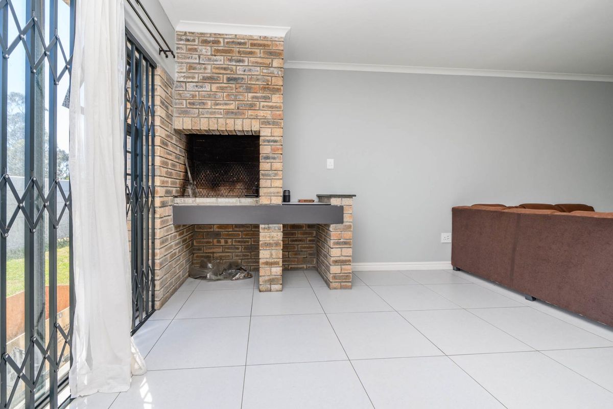 An indoor entertainment area featuring a built-in brick braai fireplace, tiled flooring, and sliding security gate access to the garden.
