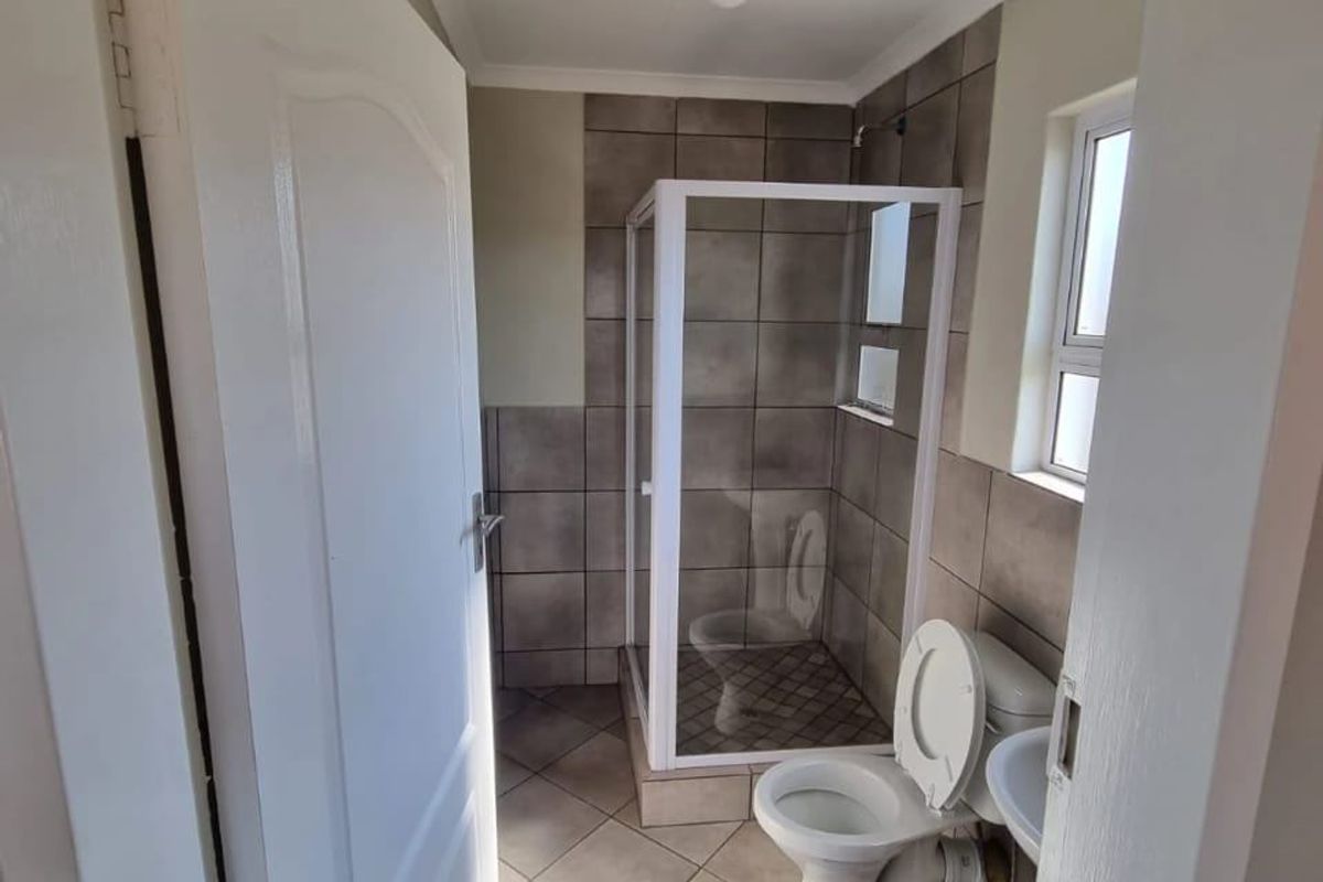 A functional bathroom featuring a glass-enclosed shower, toilet, and tiled flooring with neutral wall finishes.