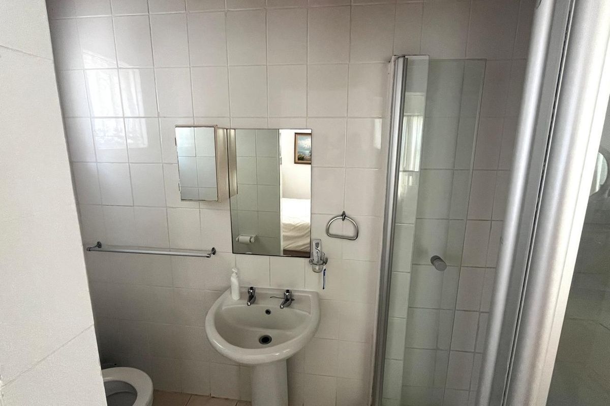 A functional bathroom featuring a pedestal sink, a glass-enclosed shower, and white wall tiling.