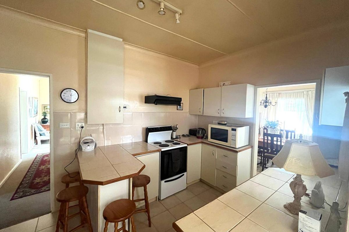 A functional kitchen featuring tiled countertops, built-in cabinetry, an electric stove with extractor fan, and a breakfast nook area.