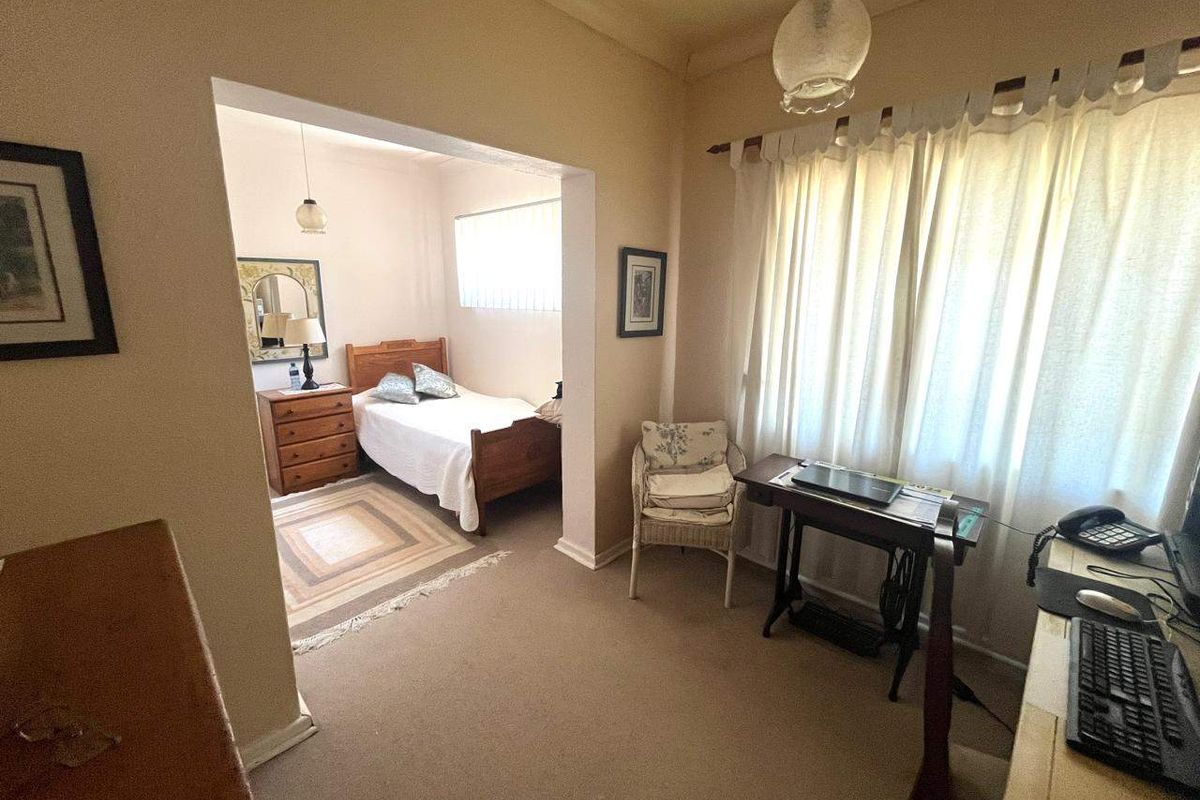 A bedroom featuring an adjoining study or sitting area, with neutral wall tones and carpeted flooring throughout.